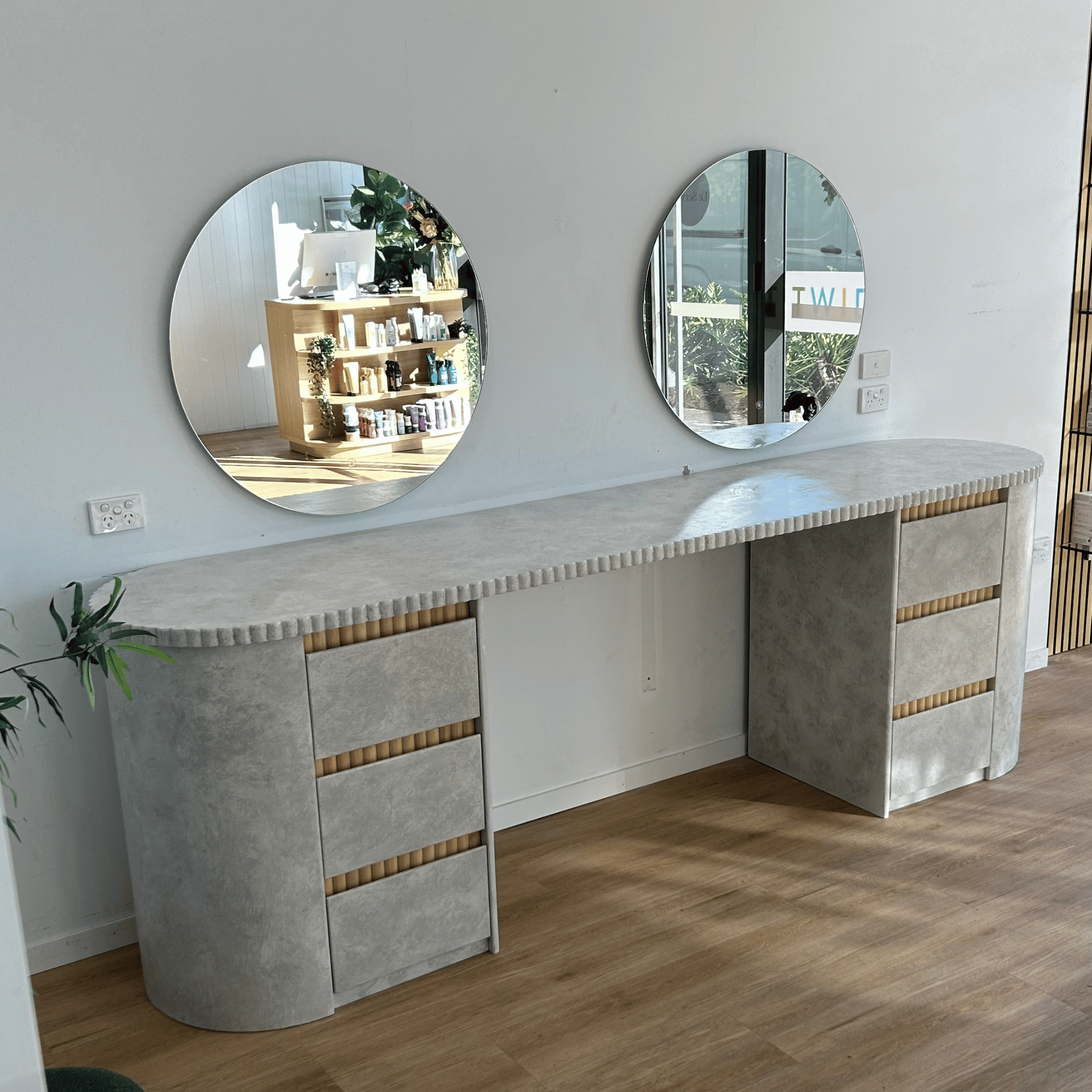 Modern vanity with round mirrors in a room with wooden flooring and a light gray wall.