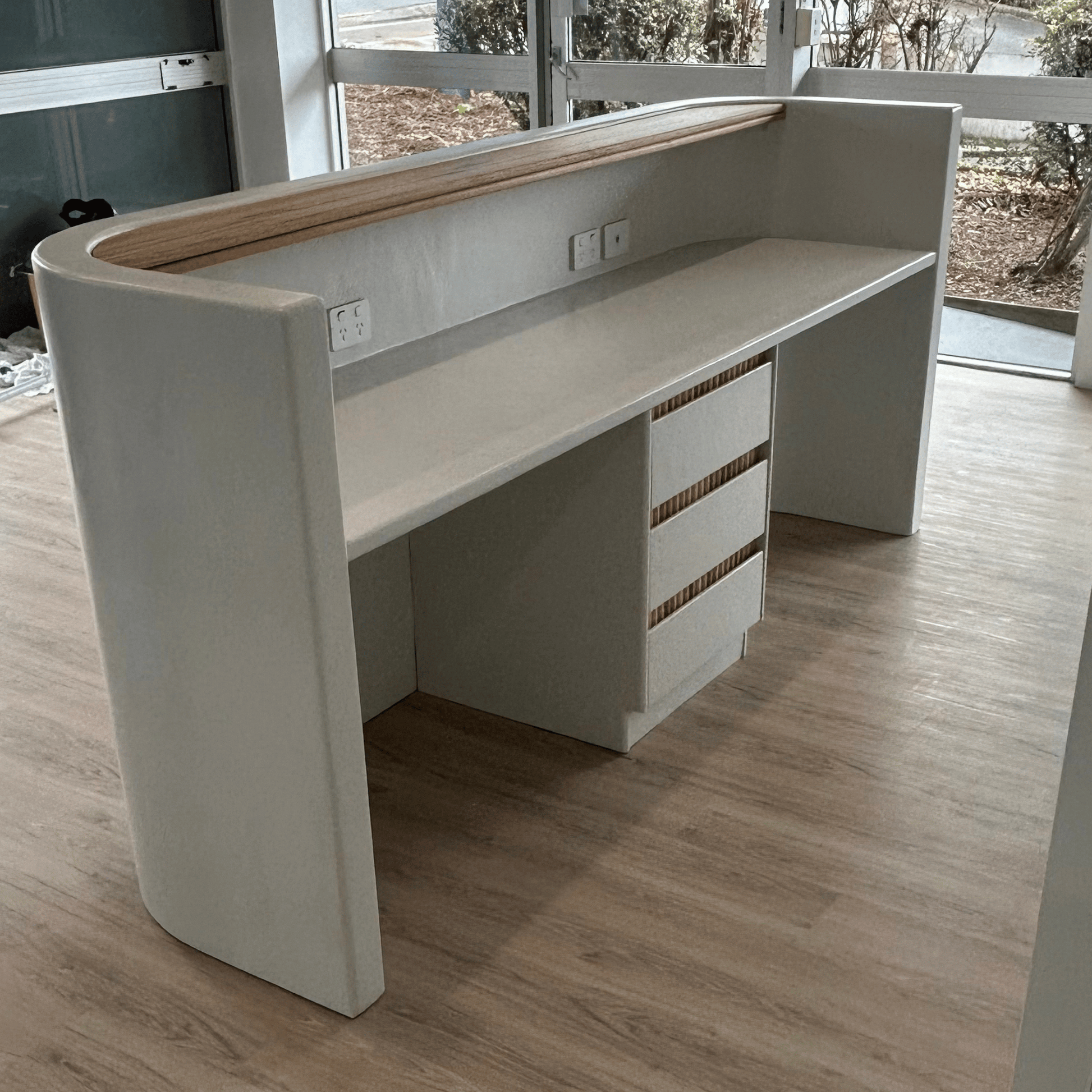 Modern white desk with wooden top in a room with large windows.