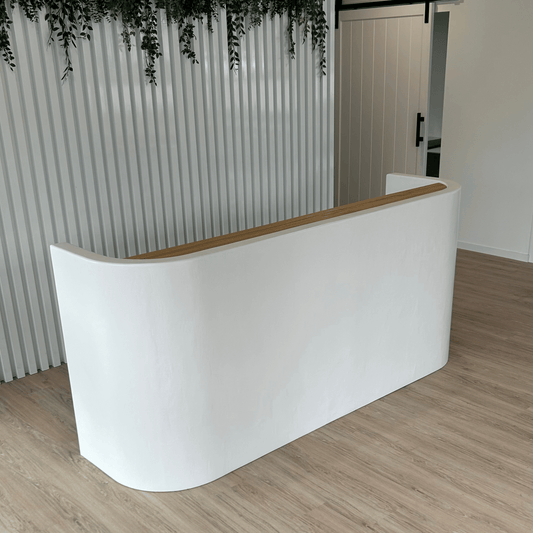 Curved white reception desk with wooden top in a room with striped wall and plants.