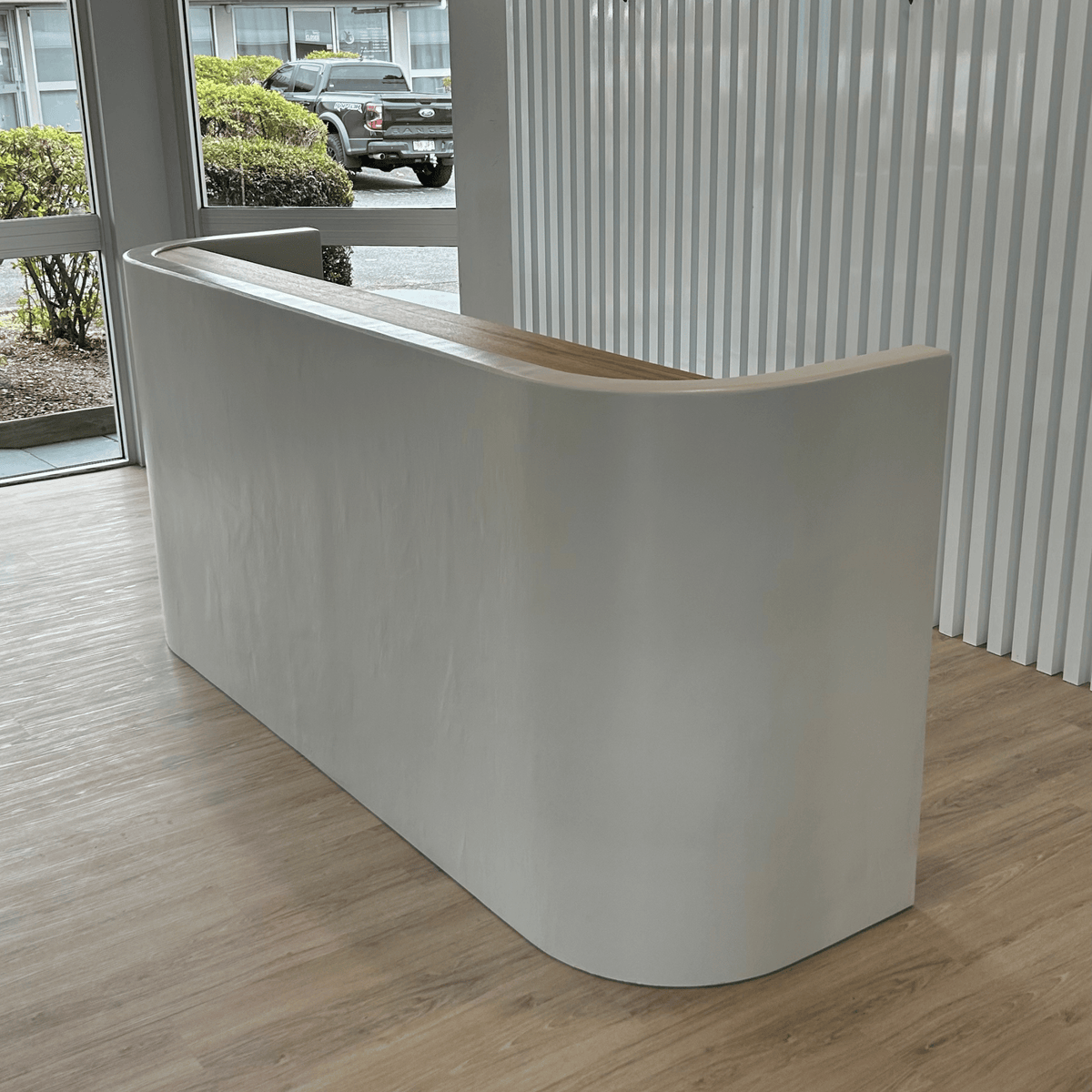 Modern reception desk in an office setting with a glass wall and outdoor view.