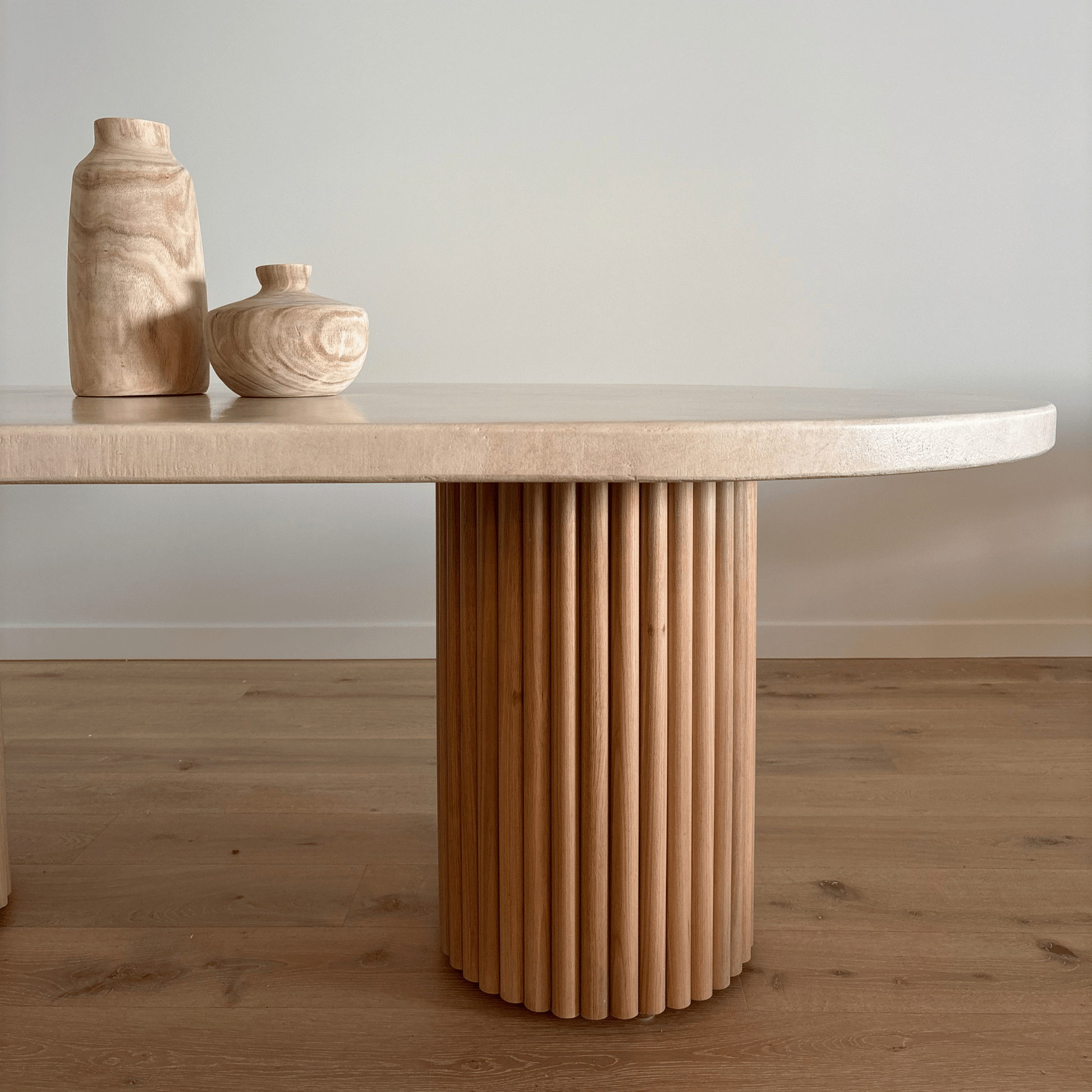 Wooden dining table with a textured cylindrical base and two wooden vases on top.